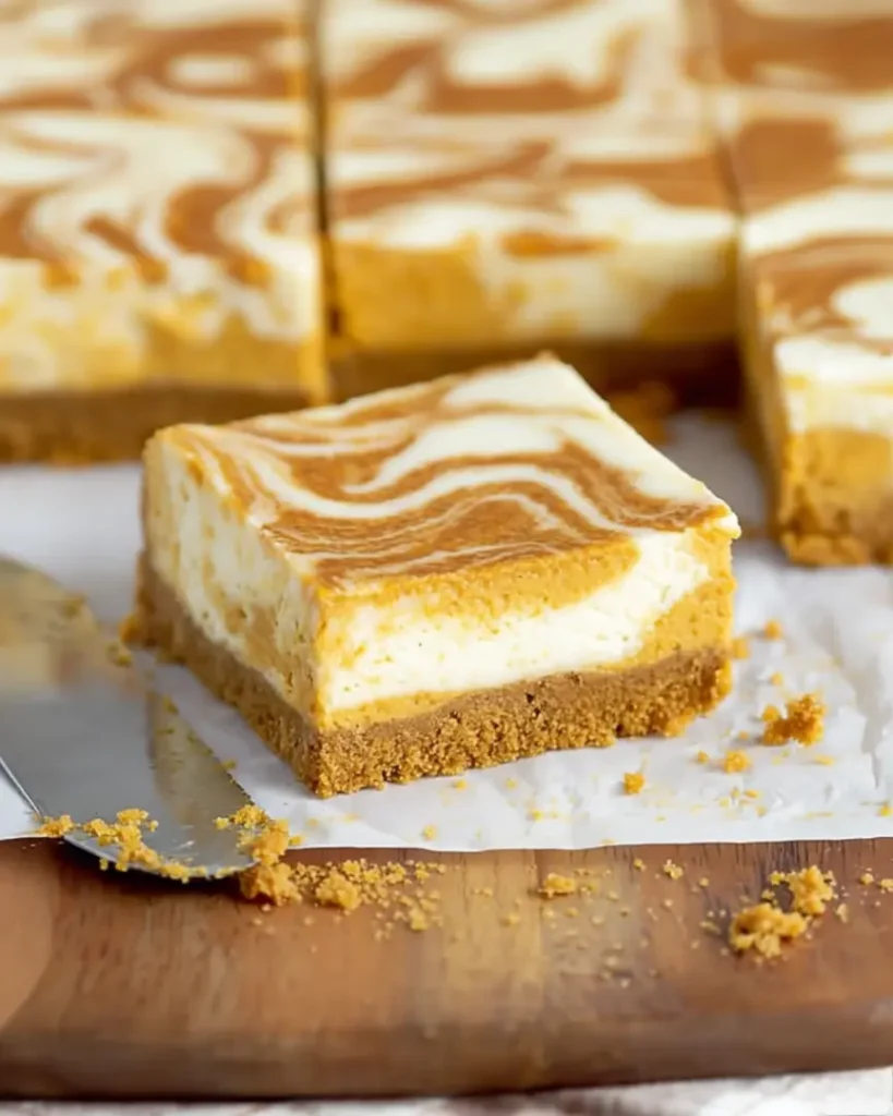 Close-up of a single pumpkin cheesecake bar with pumpkin swirl and graham cracker crust on parchment paper