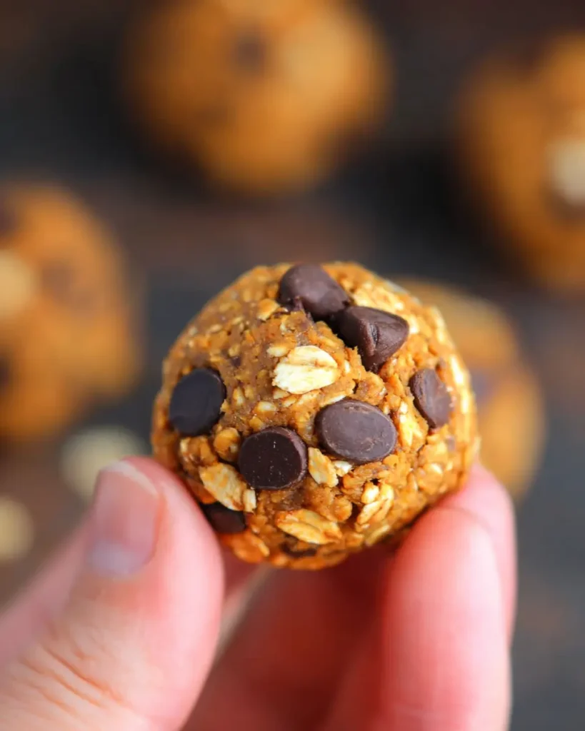 Close-up of pumpkin chocolate chip energy bite held between fingers over gray stone surface