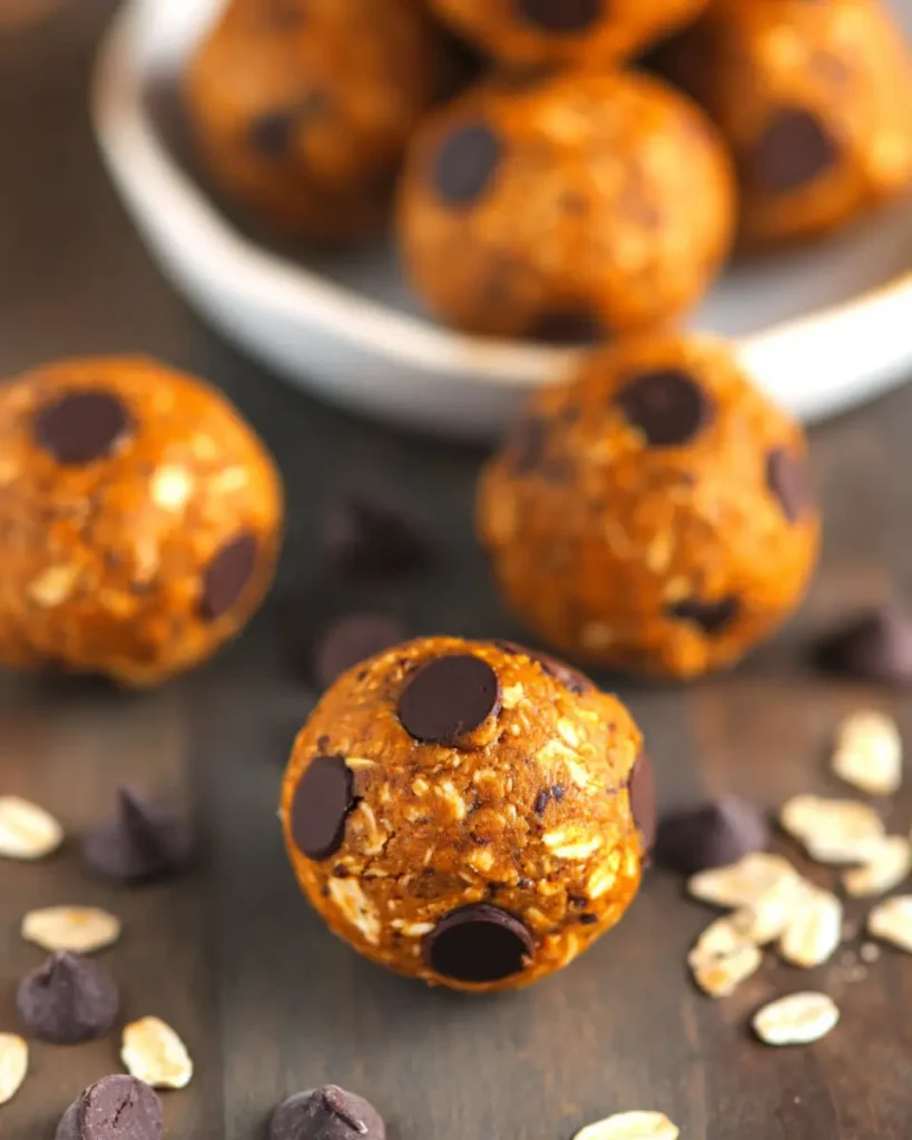 Rustic arrangement of pumpkin chocolate chip energy bites with chocolate chips and a small bowl on gray stone surface