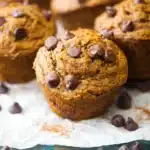 Freshly baked pumpkin chocolate chip muffins with melted chocolate chips and cinnamon dusting on parchment paper