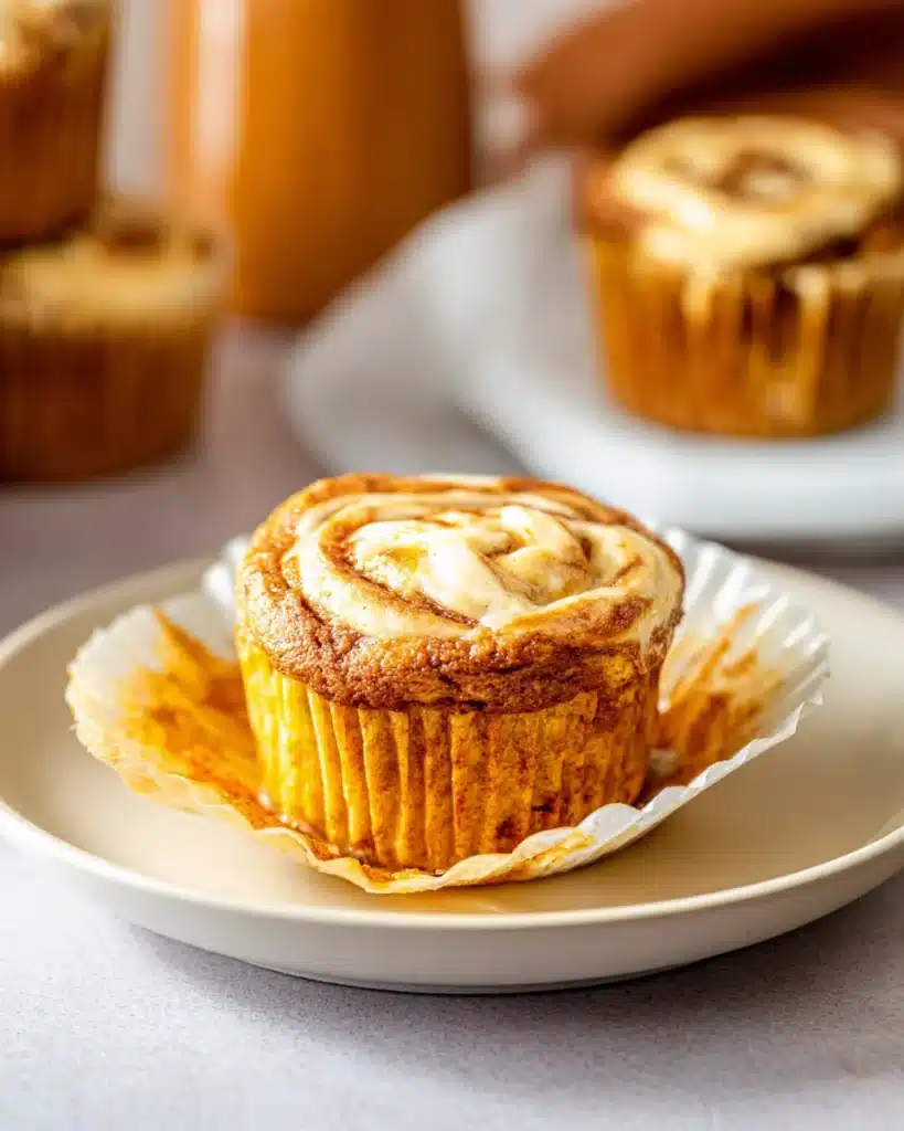 Fresh pumpkin cream cheese swirl muffin with creamy topping on white plate, unwrapped and ready to eat