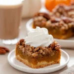 Pumpkin pecan pie bar with whipped cream on white plate, showing crunchy pecan topping, smooth pumpkin filling, and cookie crust.