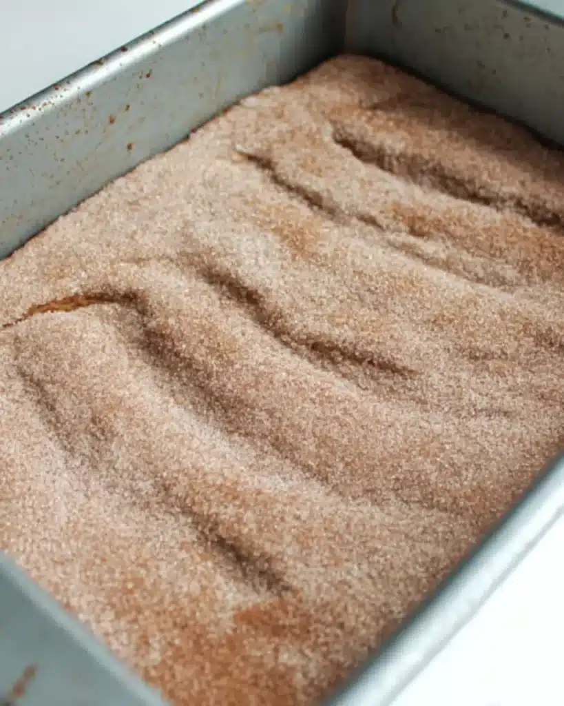 Unbaked pumpkin snickerdoodle snack cake batter topped with cinnamon sugar in a baking pan