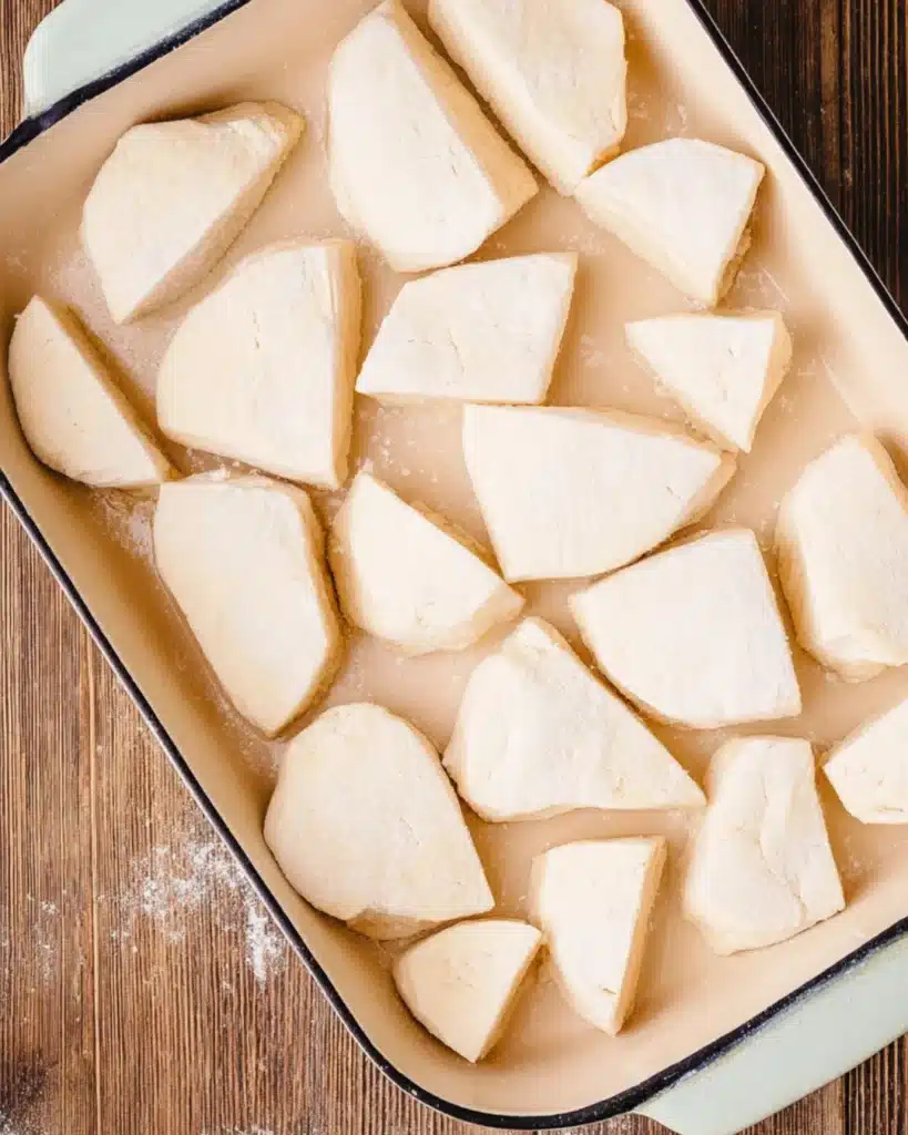 Raw biscuit dough quarters arranged in a baking dish for breakfast casserole