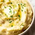 Creamy crockpot mashed potatoes with melted butter and parsley in a white bowl