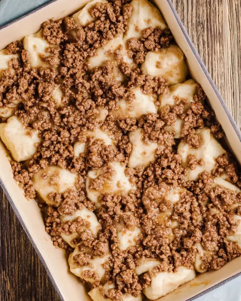 Browned ground sausage layered over raw biscuit dough in baking dish