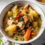 Bowl of hearty slow cooker chicken stew with carrots, potatoes, and herbs in creamy broth