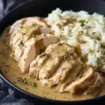 Slow Cooker Chicken and Gravy served over mashed potatoes in a black bowl with herb garnish