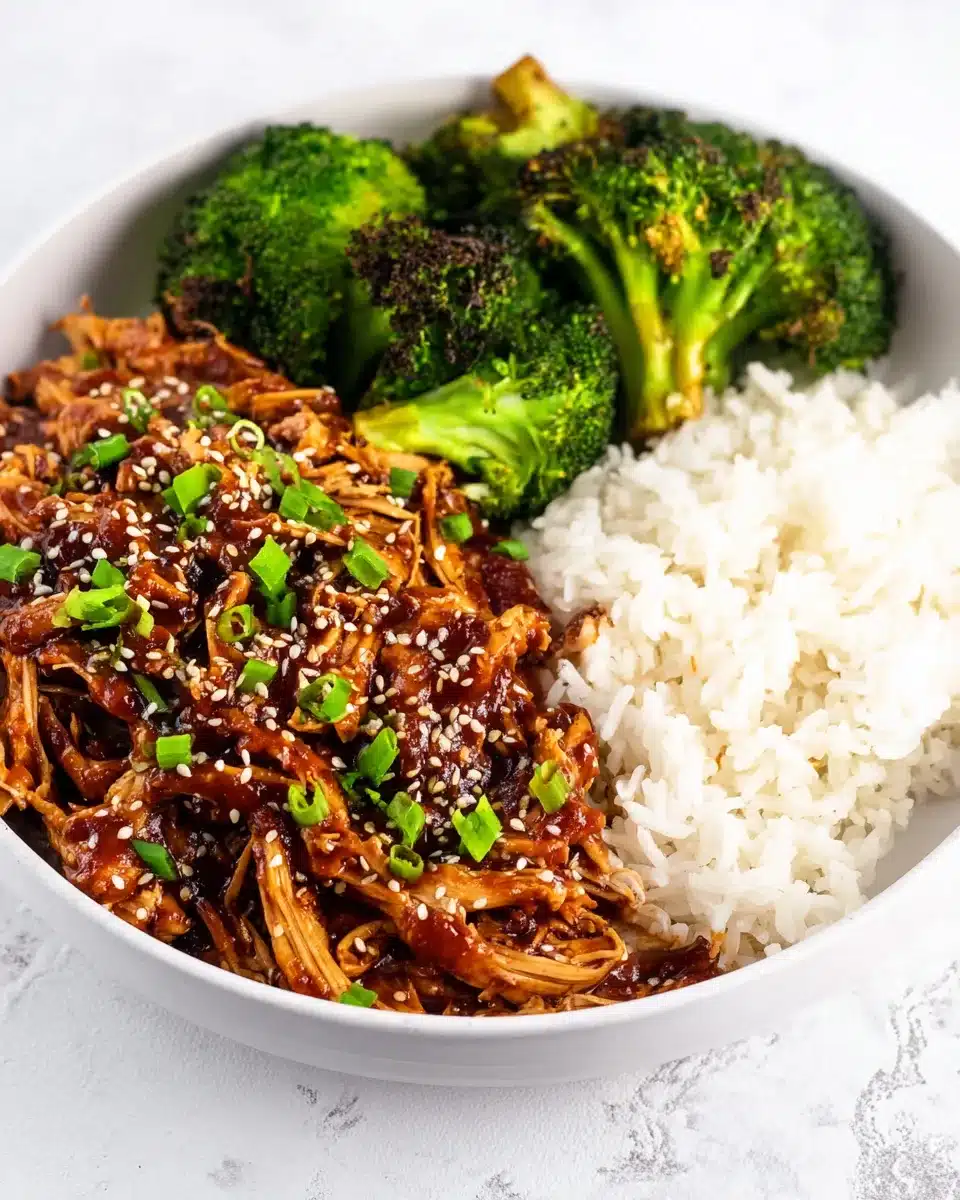 A bowl of slow cooker honey garlic chicken topped with sesame seeds and green onions, served with white rice and roasted broccoli.
