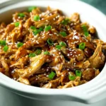 Slow cooker teriyaki chicken topped with sesame seeds and green onions in a white ceramic crockpot
