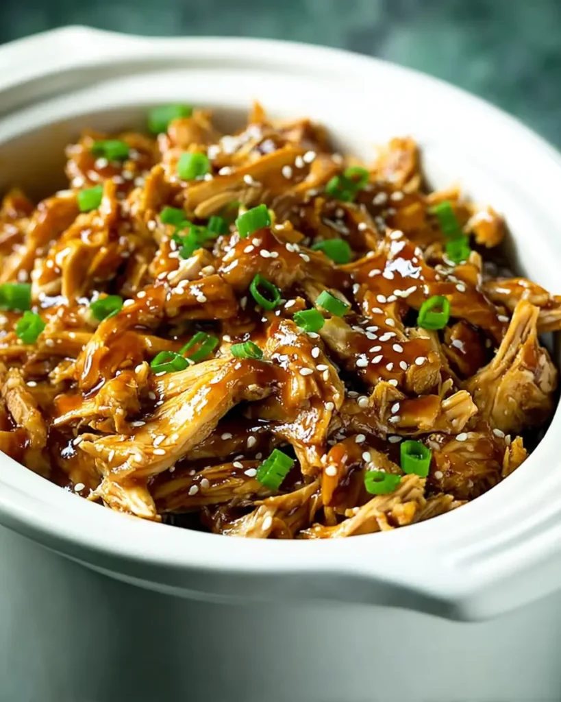 Slow cooker teriyaki chicken topped with sesame seeds and green onions in a white ceramic crockpot