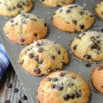 Freshly baked sour cream chocolate chip muffins in a muffin tin, topped with sparkling sugar and mini chocolate chips