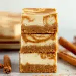 Three stacked pumpkin cheesecake bars with a swirl of pumpkin and cream cheese and a crumbly graham cracker crust on a plate