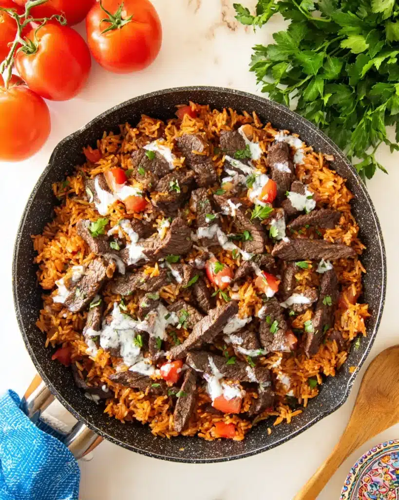 Overhead view of Steak and Queso Rice skillet with juicy steak strips, fluffy tomato rice, queso drizzle, and fresh parsley, surrounded by tomatoes and rustic table setting.