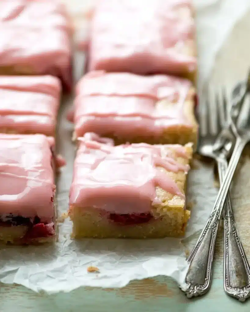 Sliced strawberry lemon blondies with pink glaze and forks on rustic table
