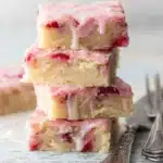 Stack of strawberry lemon blondies with pink glaze and fresh strawberries on rustic surface