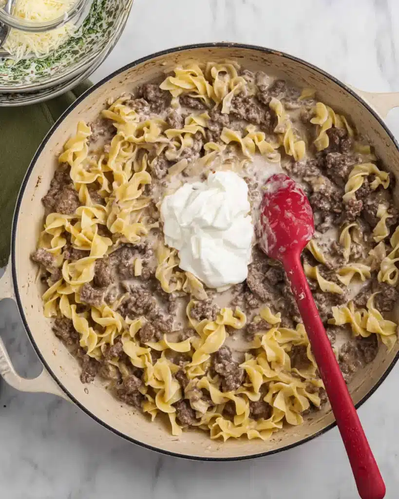 Ground beef stroganoff in skillet with sour cream added on top before mixing