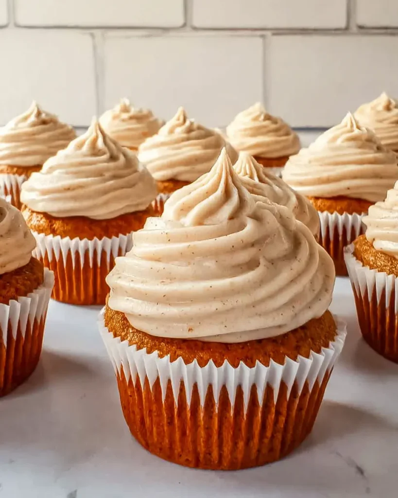 Pumpkin cupcakes in fall liners topped with swirled cinnamon cream cheese frosting