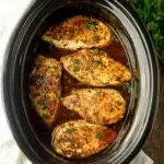Juicy slow cooker chicken breasts seasoned with herbs and served in a black ceramic crockpot with rich broth