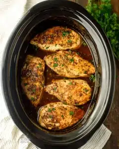 Juicy slow cooker chicken breasts seasoned with herbs and served in a black ceramic crockpot with rich broth