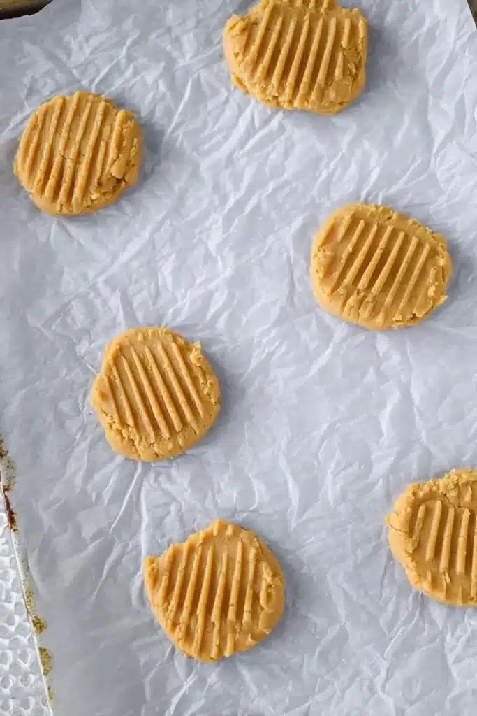Unbaked peanut butter cookie dough rounds flattened with fork marks on parchment paper