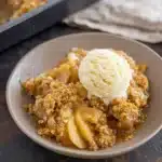 Ultimate Apple Crisp served with vanilla ice cream in a ceramic bowl on dark slate table This keeps it natural, descriptive, and SEO-friendly with "Ultimate Apple Crisp" right at the beginning.