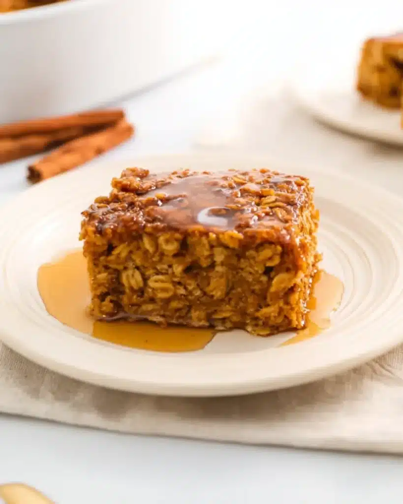 Slice of pumpkin baked oatmeal with honey drizzle on a white plate, ready to serve warm or chilled