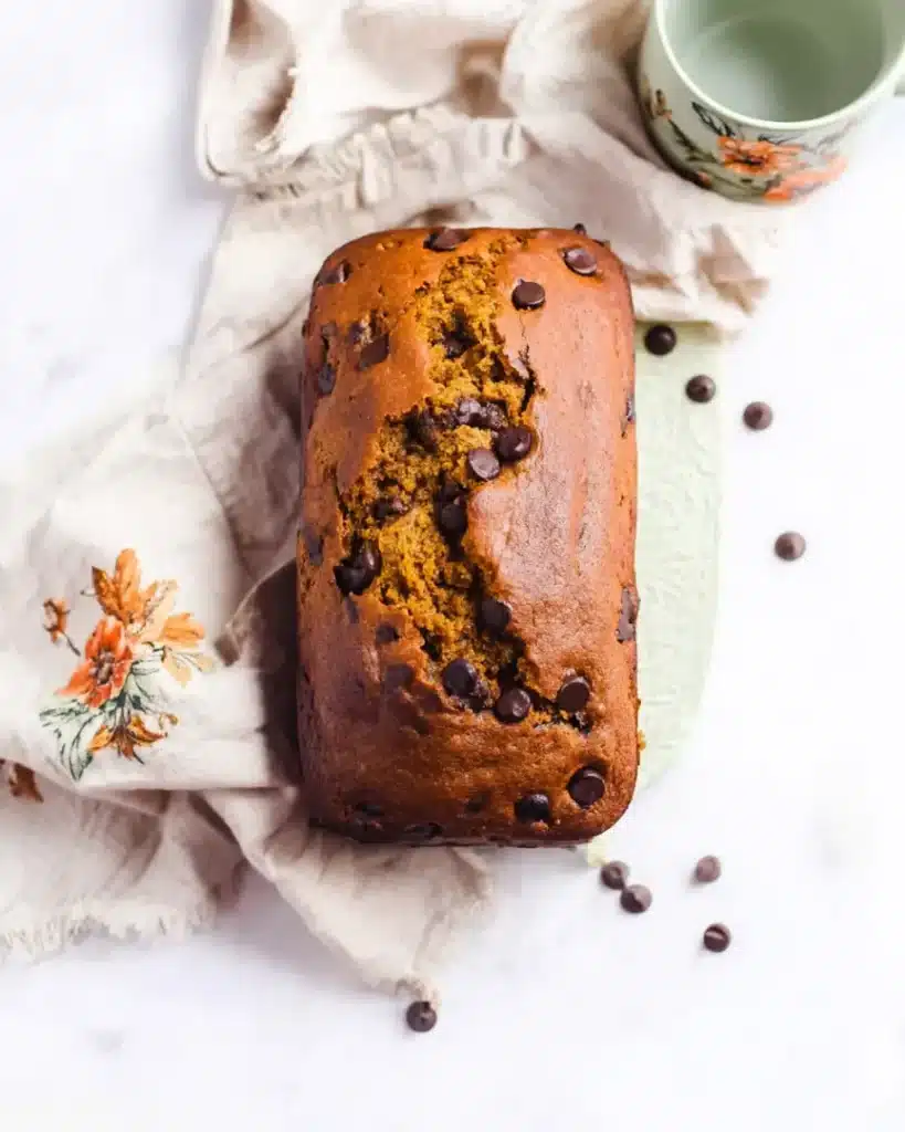 Overhead view of a full loaf of chocolate chip pumpkin bread with melty chips and crackled crust on a rustic ceramic surface.