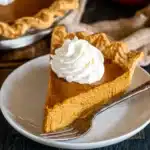 Slice of easy pumpkin pie with whipped cream on a plate with flaky crust and smooth filling.