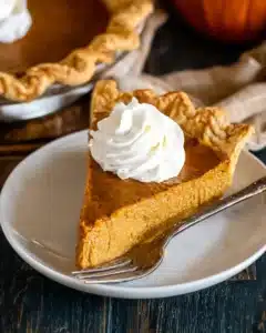 Slice of easy pumpkin pie with whipped cream on a plate with flaky crust and smooth filling.