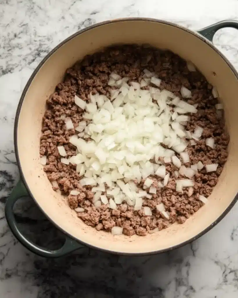 Browning ground beef with chopped onions in a Dutch oven on a kitchen counter