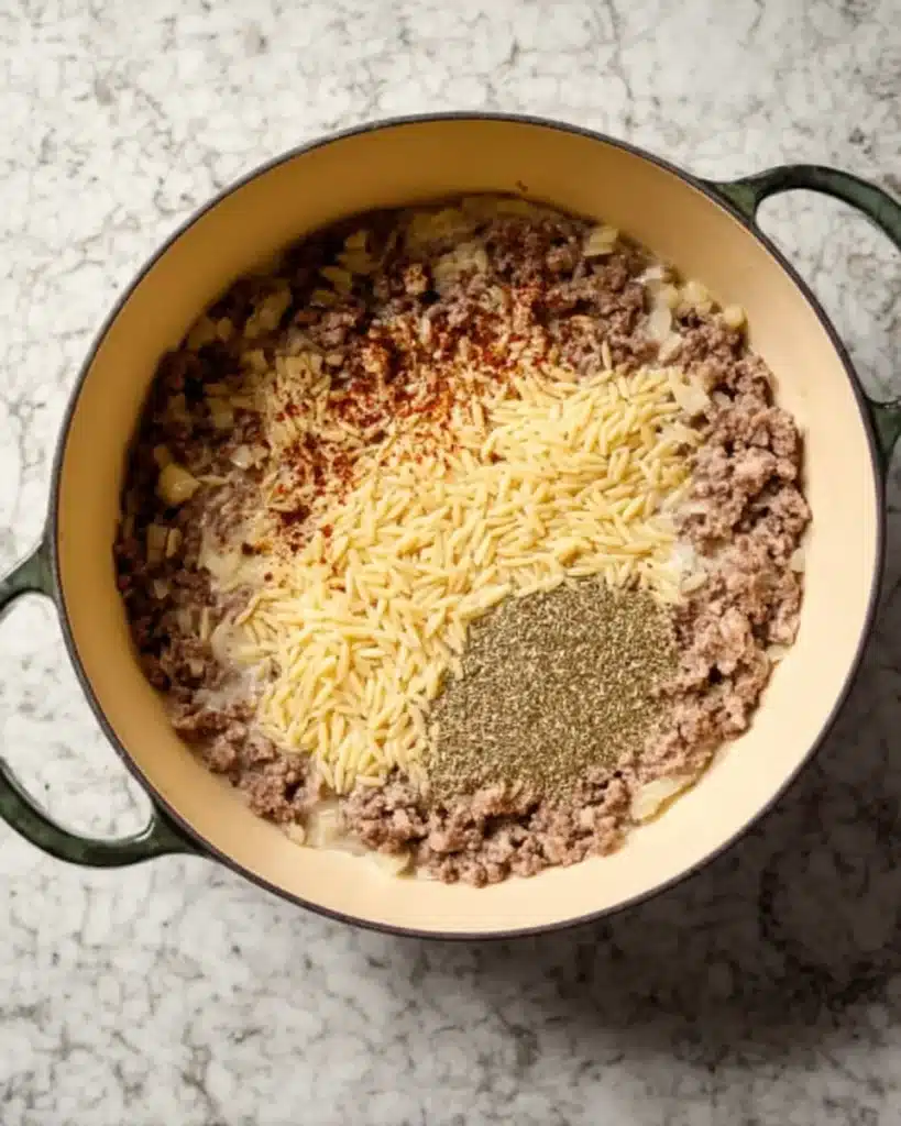 Uncooked orzo and garlic added to ground beef in Dutch oven for ground beef orzo