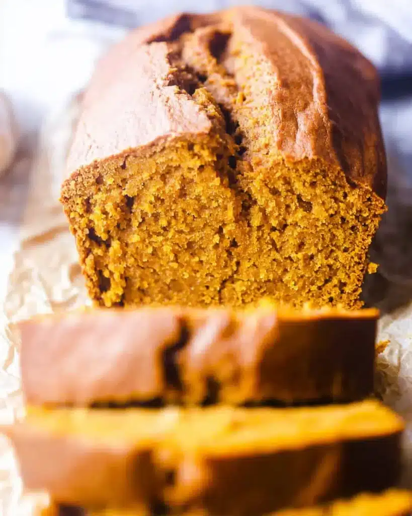 Moist slice of vanilla pudding pumpkin bread showing tender orange crumb and golden crust on parchment