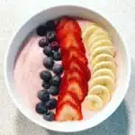 Fresh fruit smoothie bowl topped with strawberries, blueberries, and banana slices on a creamy pink base.