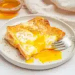 Air fryer egg and cheese toast with melted mozzarella and runny yolk on a white plate, topped with sesame seeds