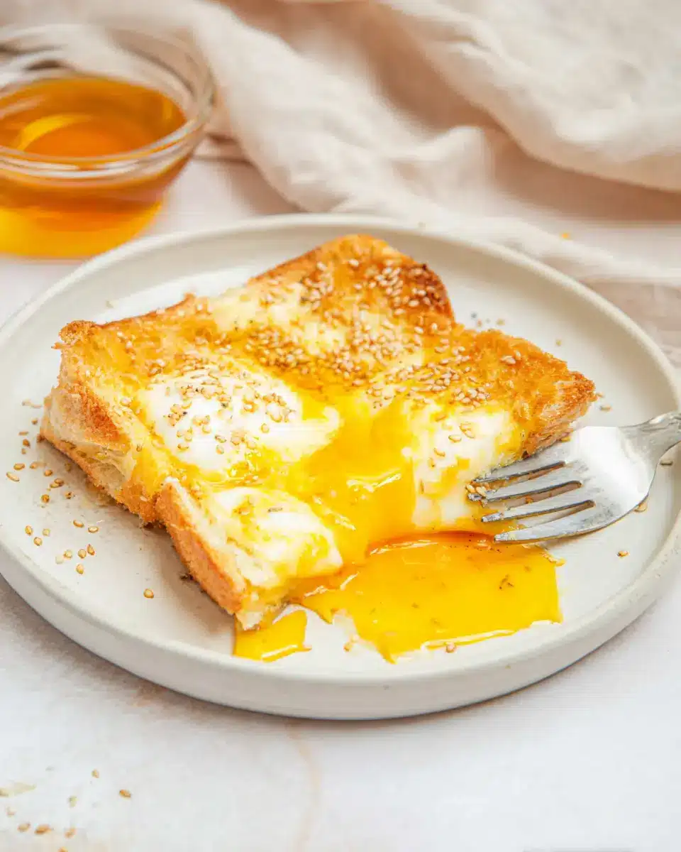 Air fryer egg and cheese toast with melted mozzarella and runny yolk on a white plate, topped with sesame seeds