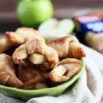 Freshly baked apple pie bites in crescent dough with green apple slices and pecans, served in a bowl lined with a napkin.