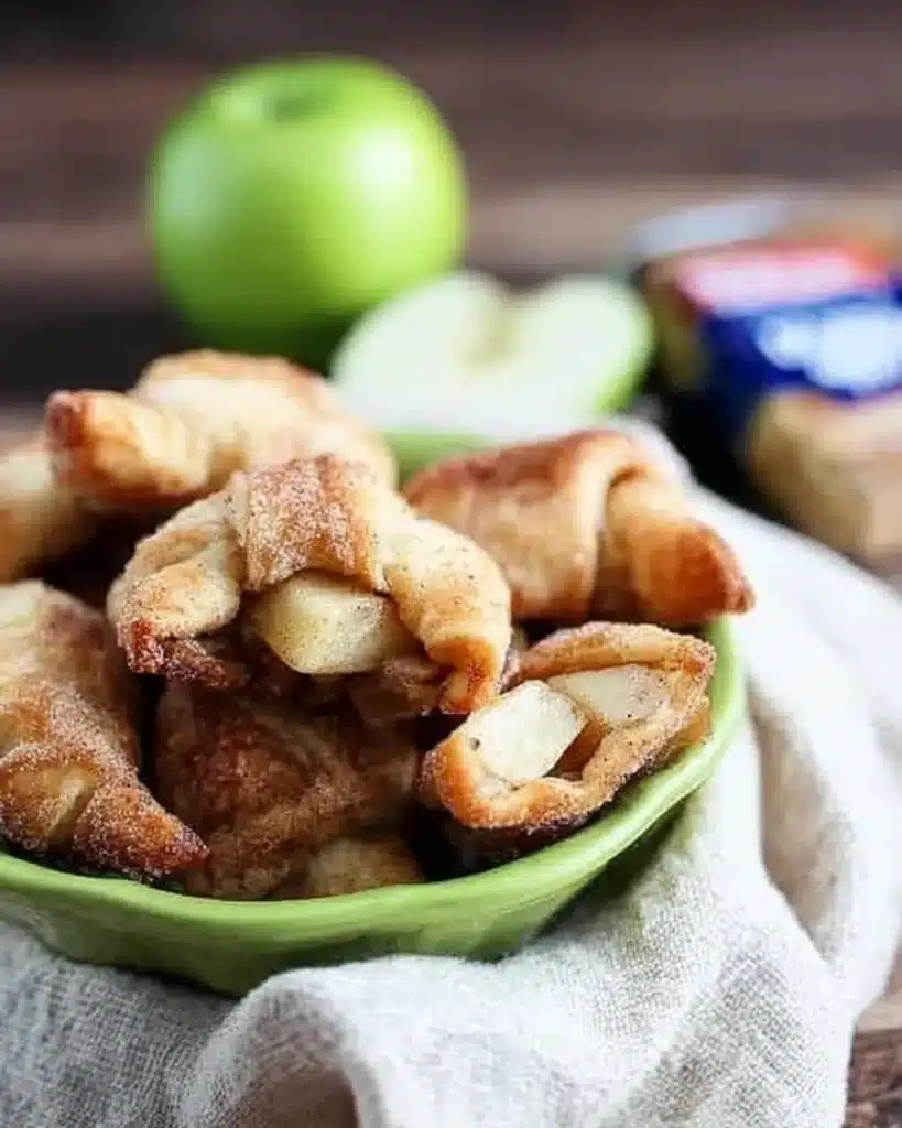 Freshly baked apple pie bites in crescent dough with green apple slices and pecans, served in a bowl lined with a napkin.