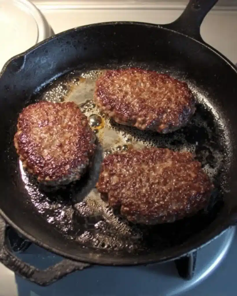 Cheeseburger Skulls patties searing in a cast-iron skillet with sizzling oil