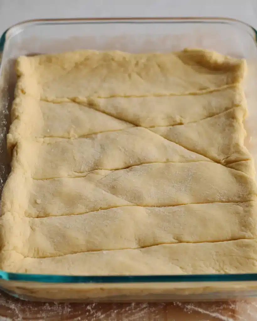 Unbaked crescent roll dough pressed in glass pan for churro cheesecake