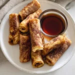 French toast rollups coated in cinnamon sugar served with maple syrup on a white plate