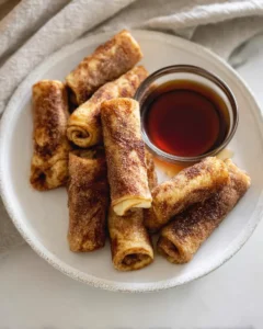 French toast rollups coated in cinnamon sugar served with maple syrup on a white plate