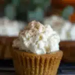 Close-up of a crustless pumpkin pie cupcake topped with whipped cream and cinnamon on a rustic table