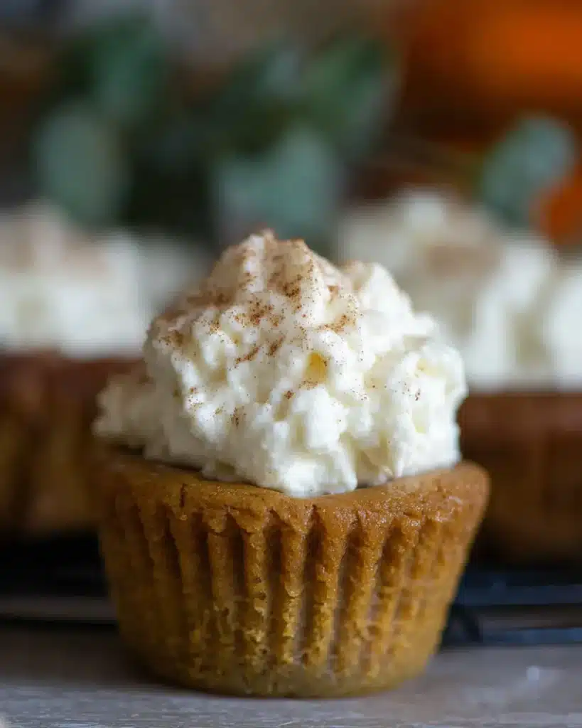 Close-up of a crustless pumpkin pie cupcake topped with whipped cream and cinnamon on a rustic table
