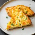 Golden egg and cheese toast slices topped with herbs on a ceramic plate