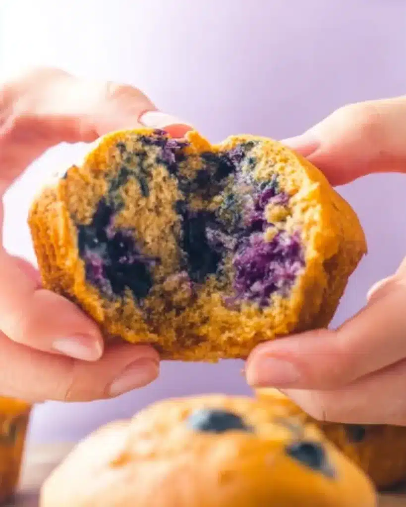 Hands gently pulling apart a fluffy blueberry muffin to reveal a soft golden crumb and juicy berries inside