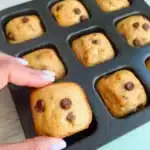 Hand lifting a mini chocolate chip banana bread from a square muffin tin.