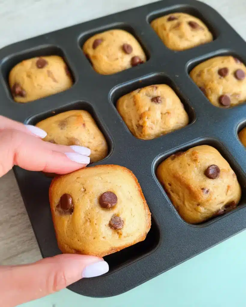 Hand lifting a mini chocolate chip banana bread from a square muffin tin.
