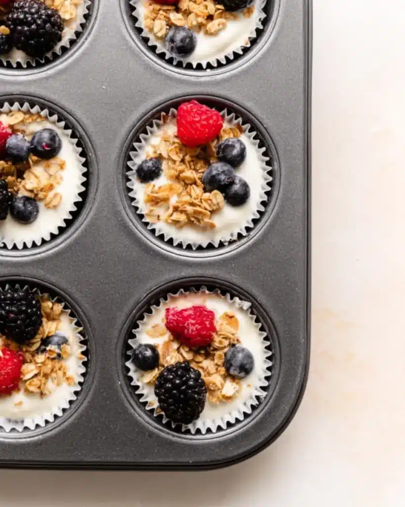 Frozen yogurt granola cups in a muffin tin with berries and granola topping.