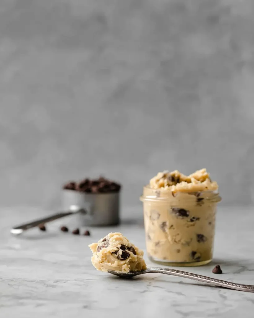 Easy Edible Cookie Dough in a glass jar with spoonful and chocolate chips on a marble surface